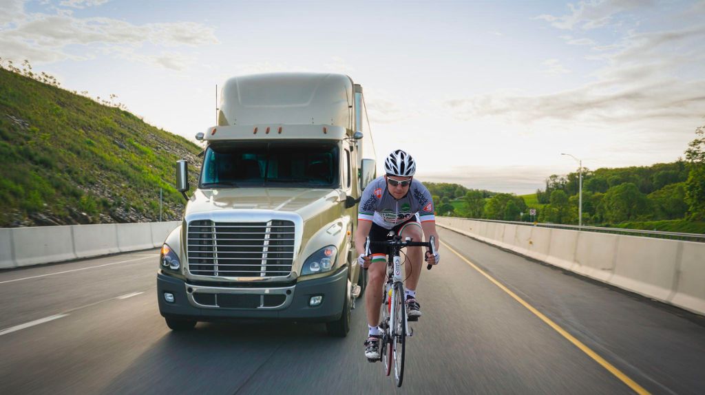 A satire photoshopped image of a person riding a bike on the highway in front of a semi-truck